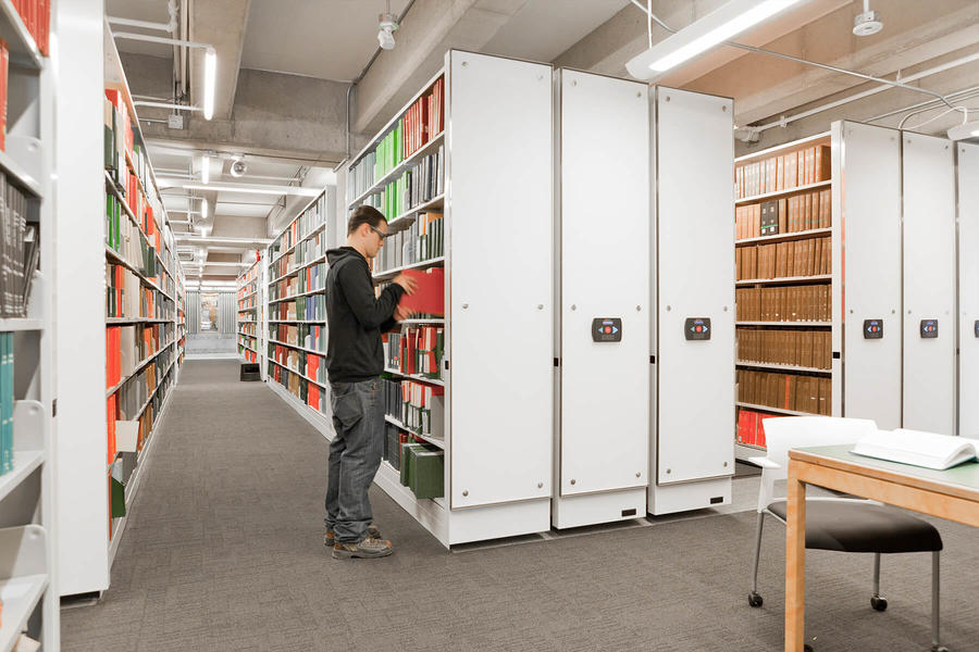 A man accesses mobile shelves in a library to consult a book.