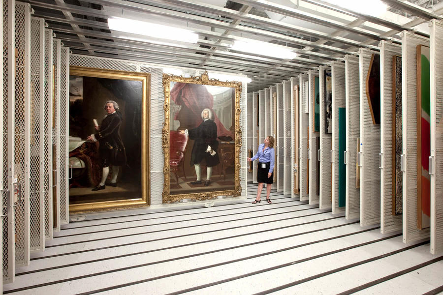 "Woman observing large historical paintings in storage. "