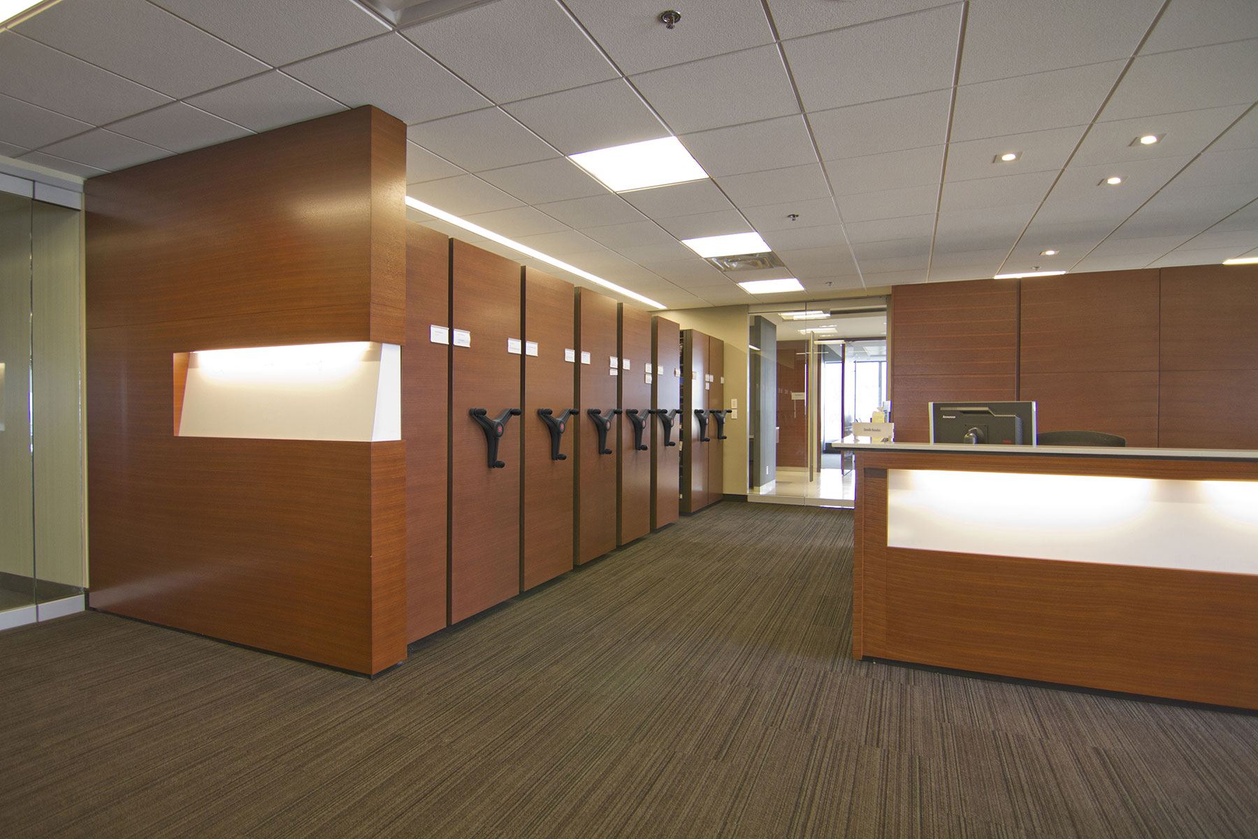 Office space featuring Montel mobile shelving system with wood finish and black hand cranks.