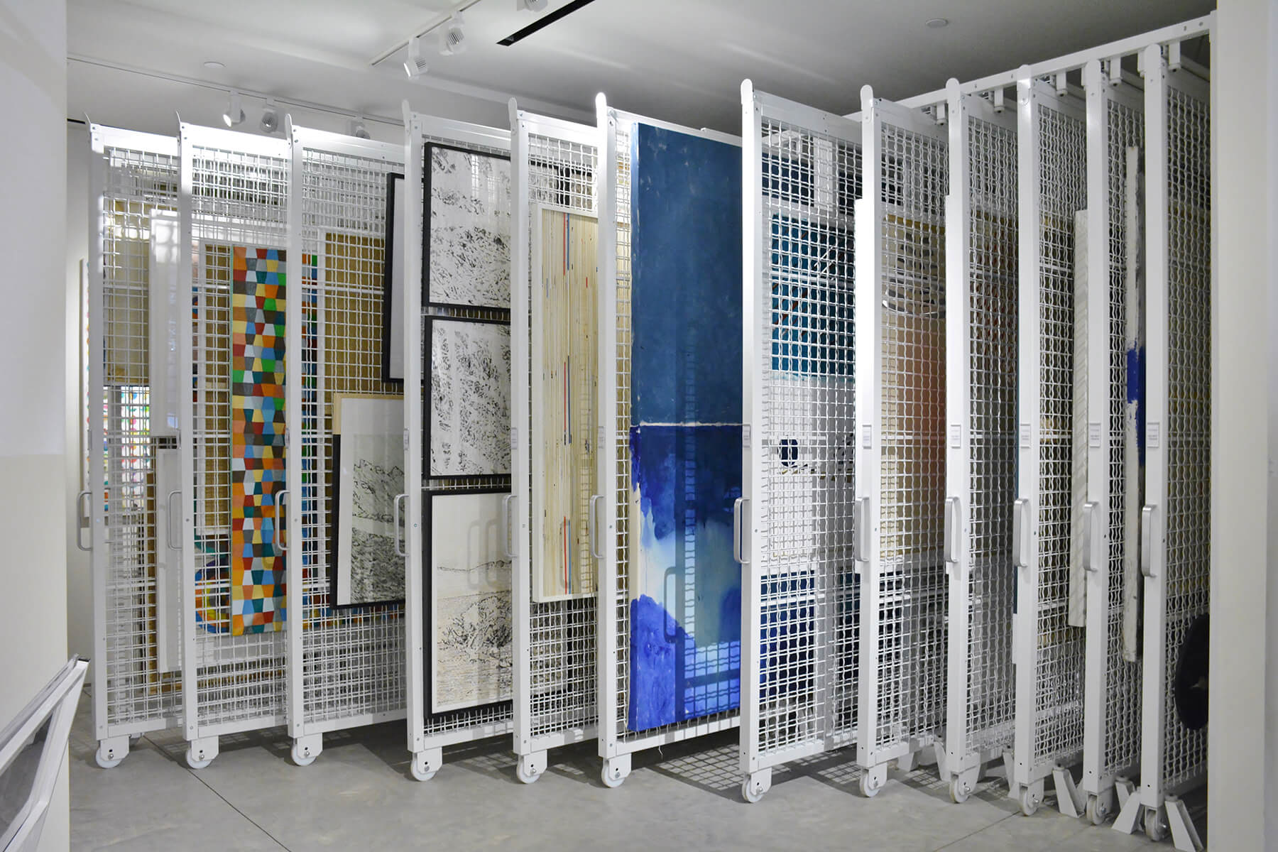 View of mobile white shelves containing various paintings, illustrating a practical art storage method.