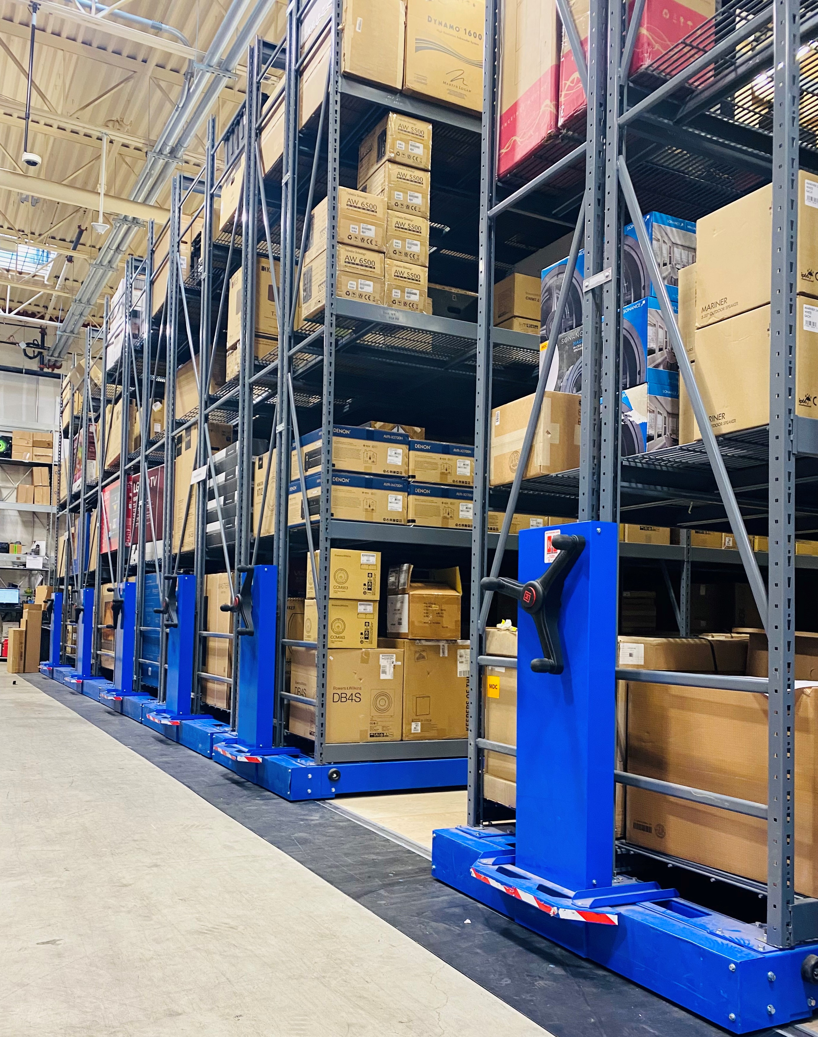 Montel mobile shelving system with industrial racks and blue hand cranks, used for warehouse box storage.