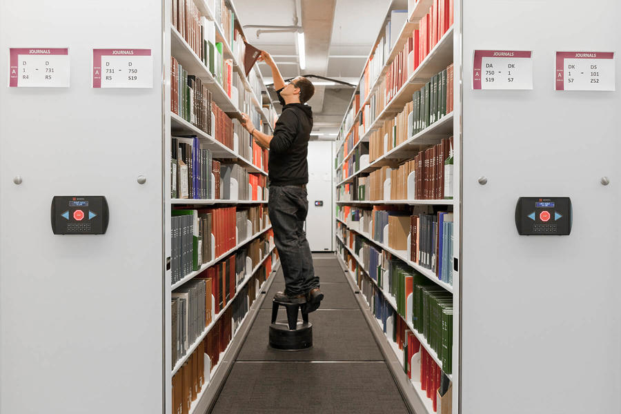 Un hombre accede a estanter&#237;as m&#243;viles en una biblioteca para consultar un libro.