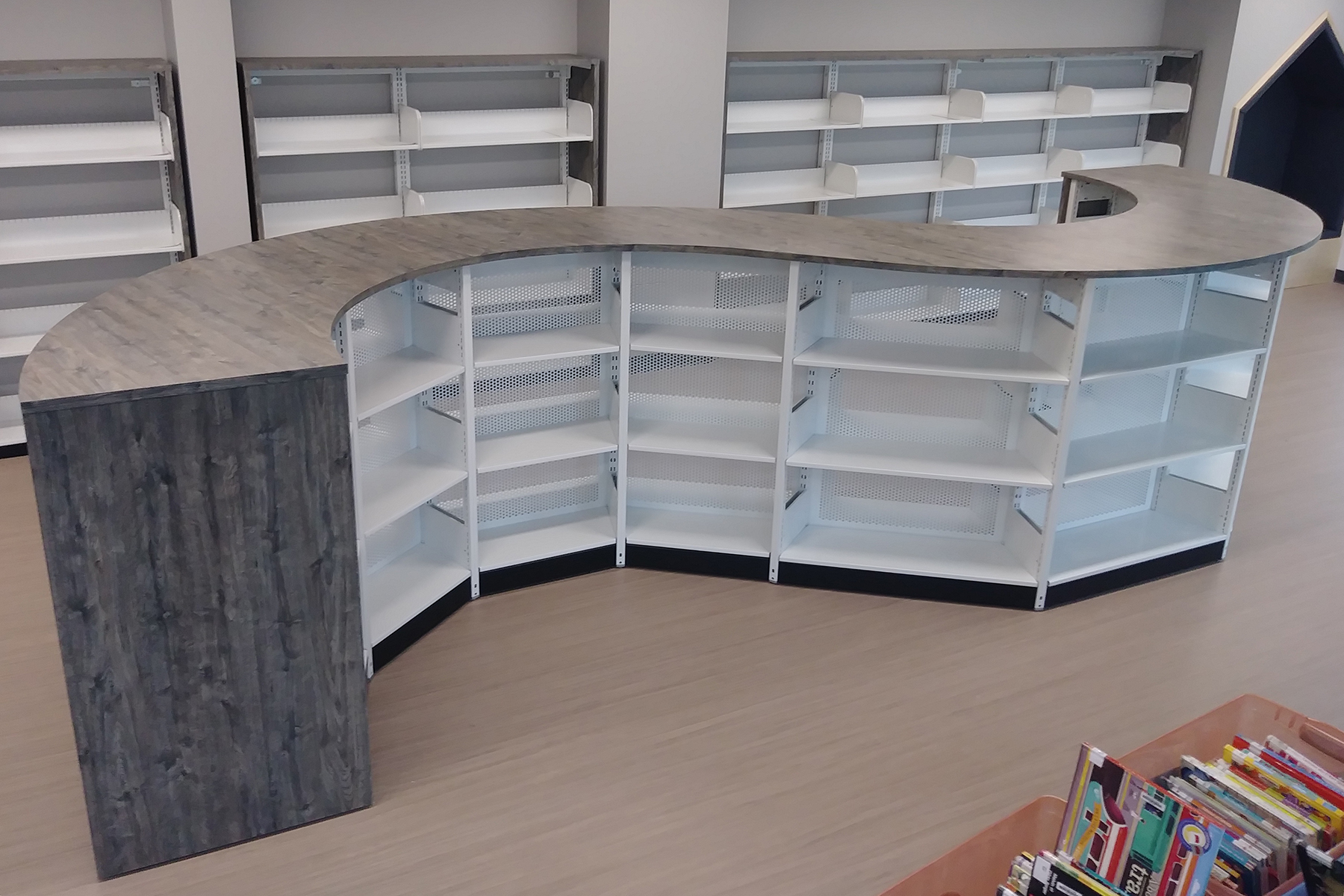 Wooden library counter with open white shelving for storage in a modern space.