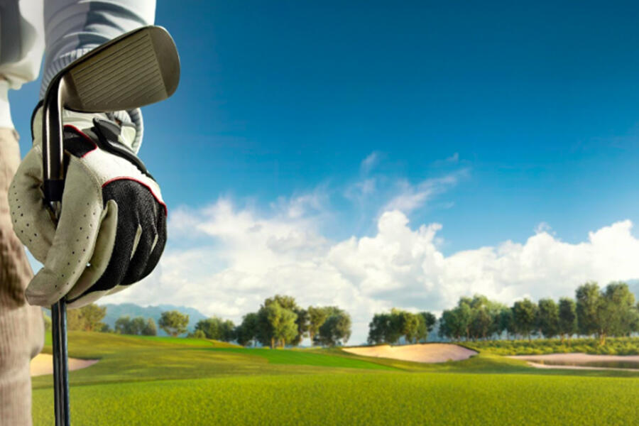 Golfista sosteniendo un palo con vista de un campo de golf al fondo.