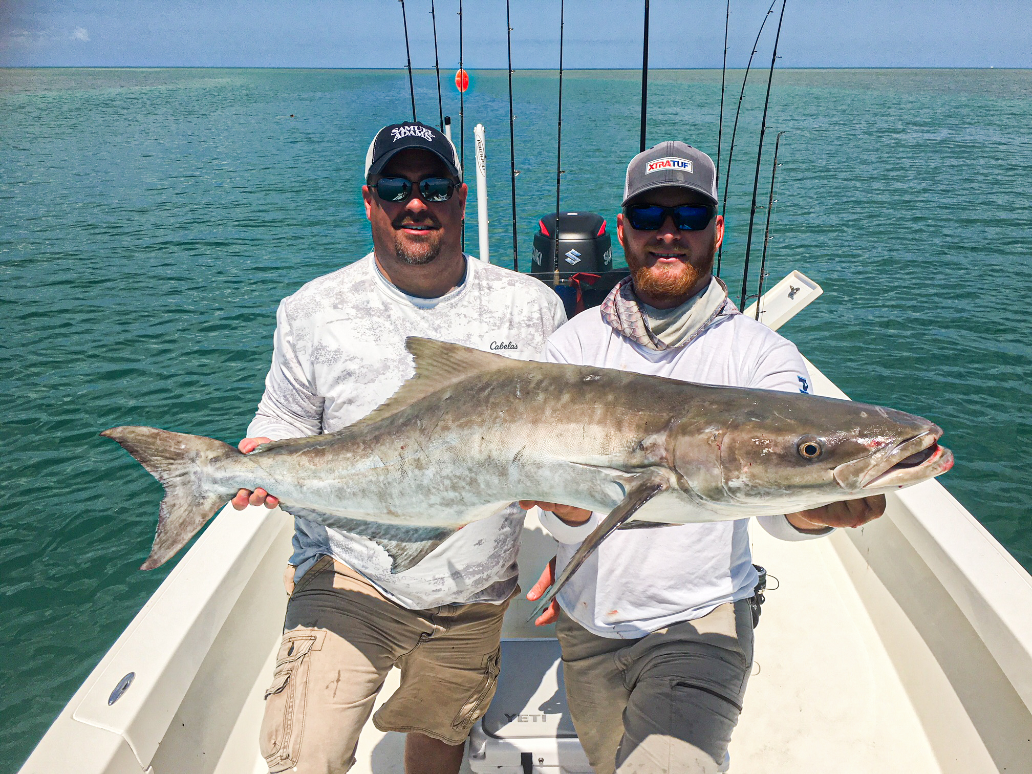 Two fishermen holding a large fish on a boat at sea.