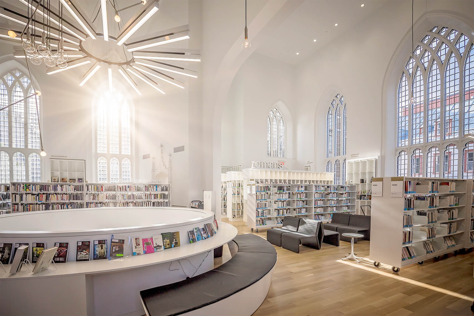 Modern library with circular shelving and large arched windows.