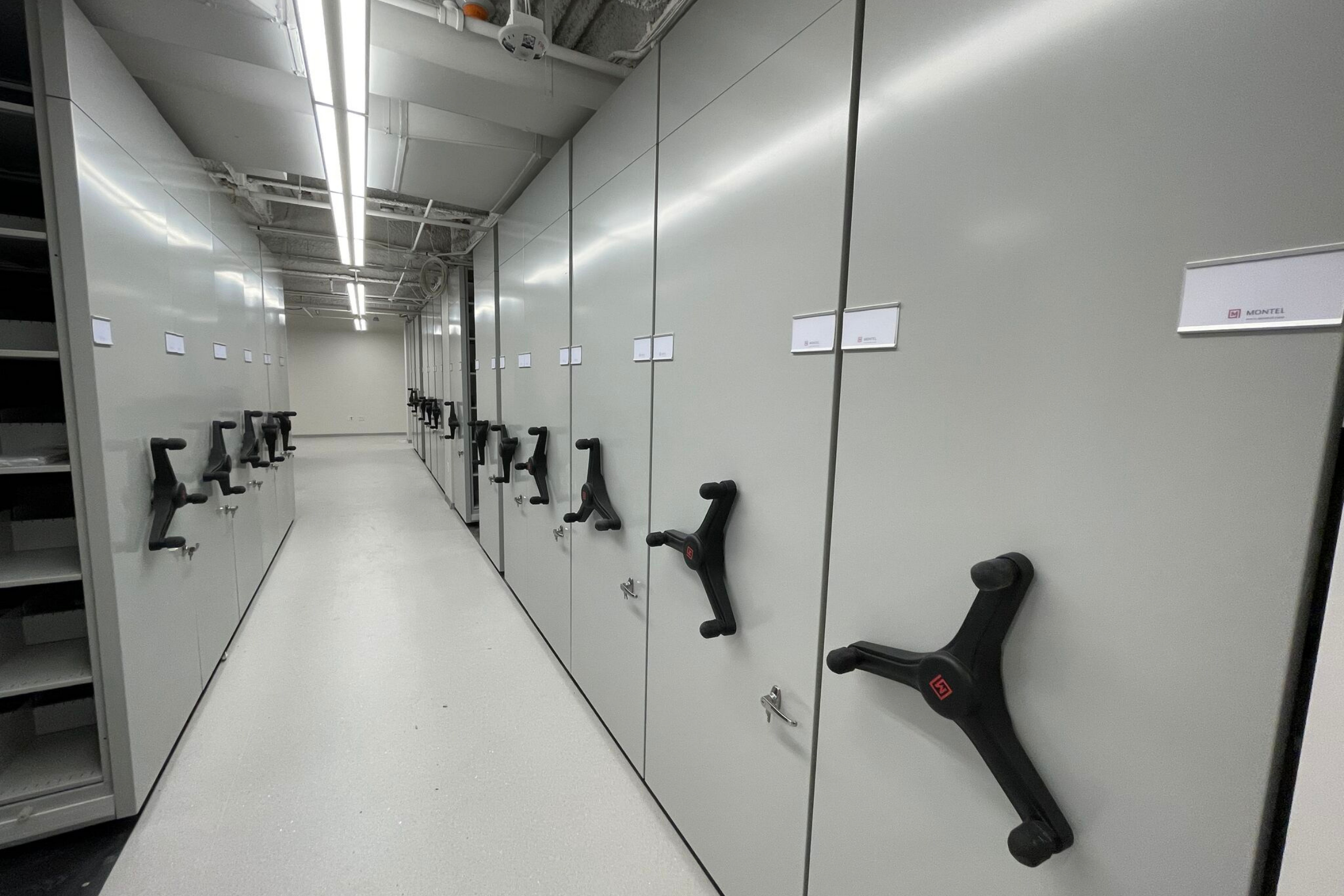 Closed mobile shelving with hand cranks in a secure storage area.