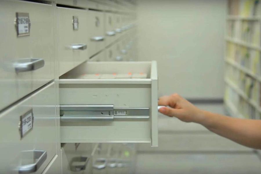 Pasillo entre dos filas de sistemas de almacenamiento con cajas de archivo y puertas de vidrio.