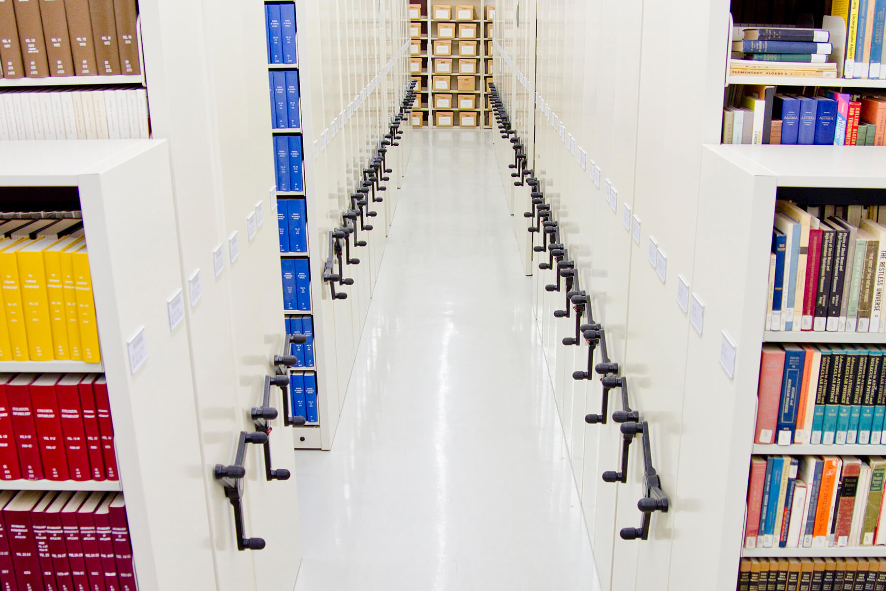 Aisle of empty shelves with handles for mobile adjustment in a storage facility.