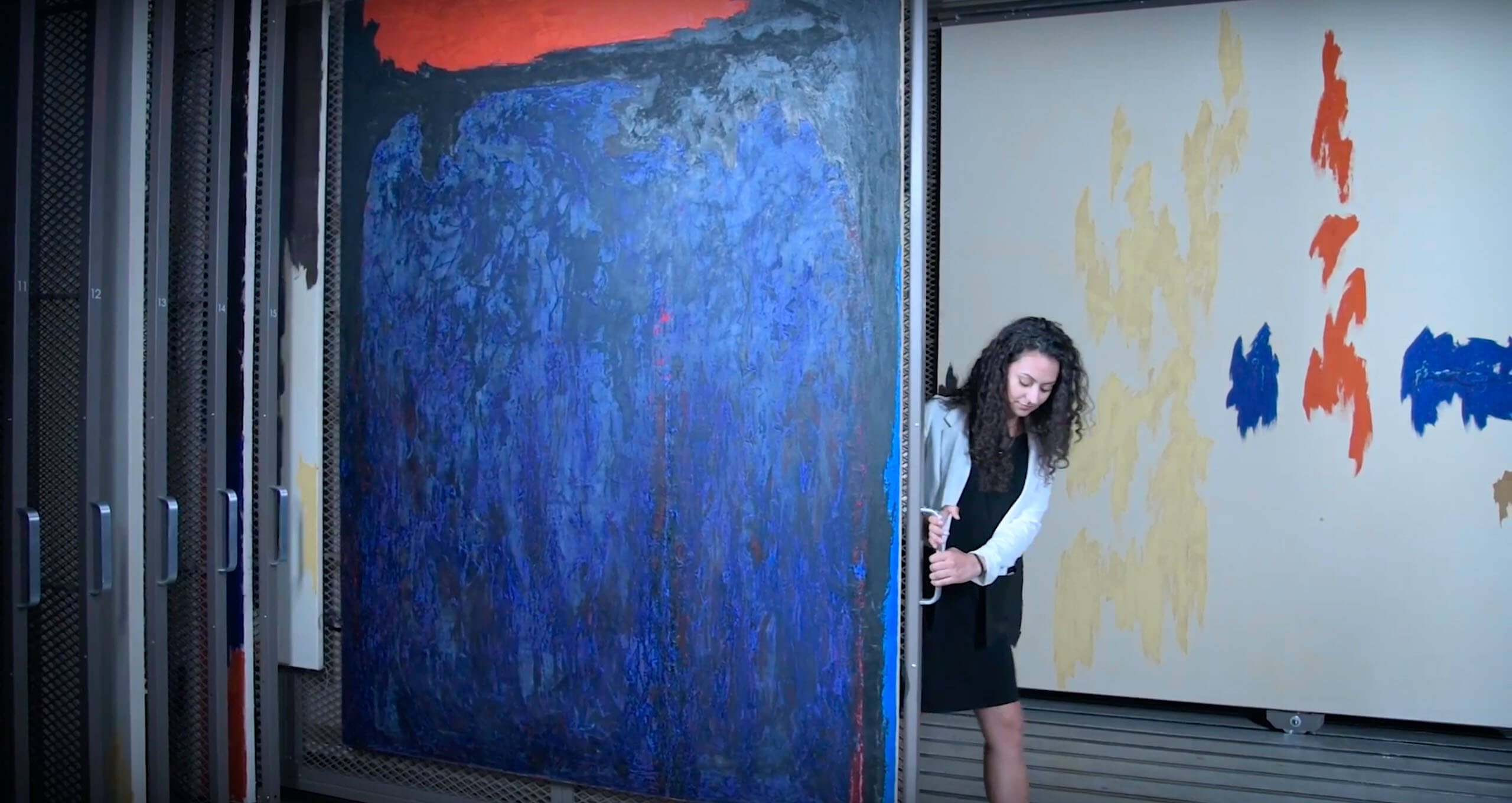 A woman opening a door to access a large canvas in a storage area, illustrating the use of storage systems.