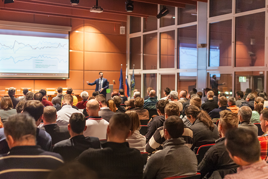 Conference with a speaker presenting graphs to an attentive audience.