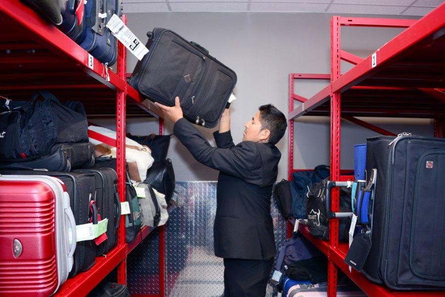 Employee accessing luggage stored on red storage shelves.